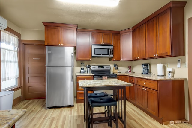 kitchen with appliances with stainless steel finishes, light stone countertops, light hardwood / wood-style floors, and a breakfast bar area