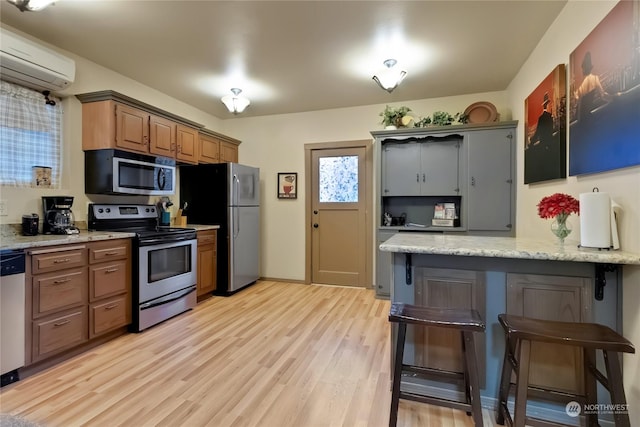 kitchen featuring appliances with stainless steel finishes, light stone counters, light hardwood / wood-style floors, a kitchen bar, and an AC wall unit