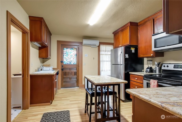 kitchen with light wood-type flooring, a wall mounted AC, stainless steel appliances, light stone countertops, and a textured ceiling