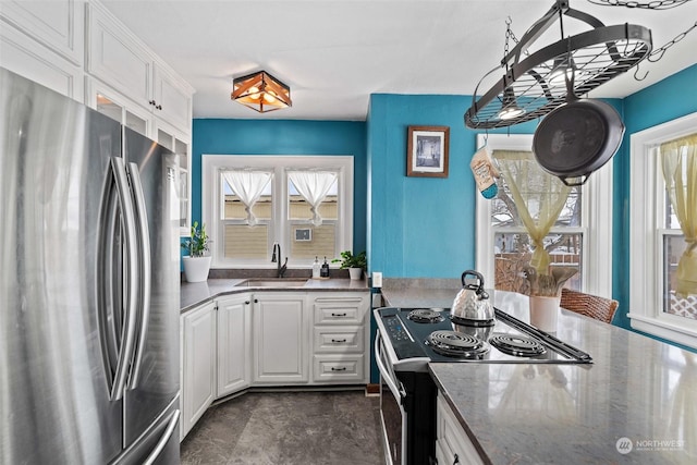 kitchen with white cabinetry, sink, electric range, stainless steel fridge, and dark stone counters