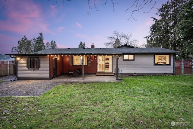 back house at dusk featuring a patio area and a yard