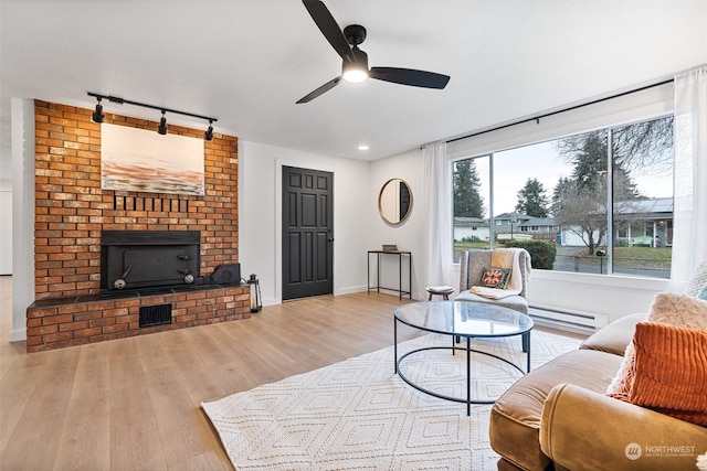 living room with a baseboard heating unit, a brick fireplace, rail lighting, ceiling fan, and light hardwood / wood-style flooring