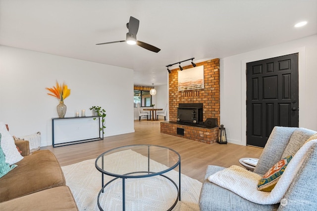 living room featuring ceiling fan, rail lighting, a fireplace, and light hardwood / wood-style floors