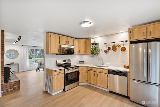 kitchen with appliances with stainless steel finishes, decorative backsplash, a wood stove, light hardwood / wood-style flooring, and sink