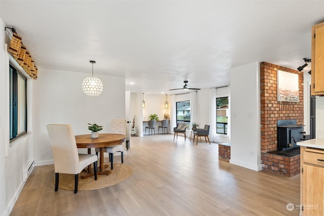 dining space with a baseboard heating unit, ceiling fan, a wood stove, and light hardwood / wood-style flooring