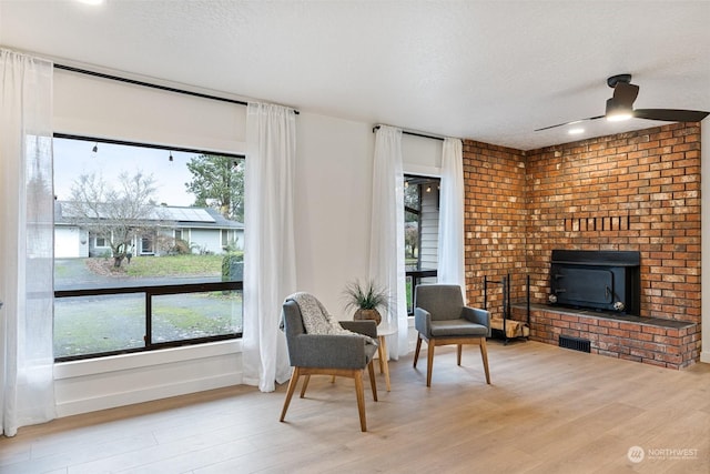 living area featuring a textured ceiling, ceiling fan, hardwood / wood-style flooring, and a brick fireplace