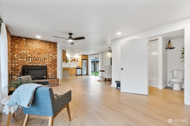 living room featuring light wood-type flooring, ceiling fan, and a fireplace