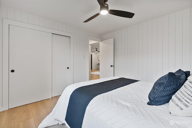 bedroom featuring ceiling fan, light hardwood / wood-style floors, a closet, and wood walls