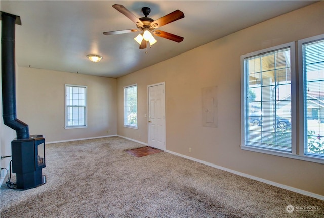 unfurnished living room with electric panel, light colored carpet, a wood stove, and ceiling fan