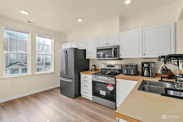 kitchen with light wood-type flooring, white cabinetry, sink, and appliances with stainless steel finishes