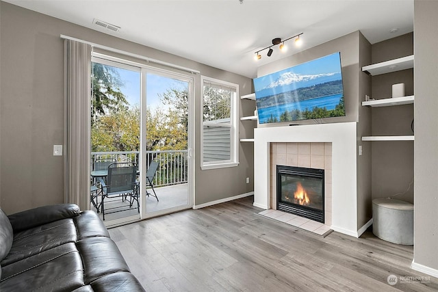 unfurnished living room featuring a fireplace, built in shelves, track lighting, and light hardwood / wood-style flooring