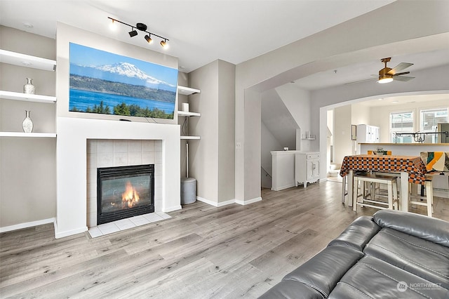 living room with built in shelves, ceiling fan, a fireplace, and light wood-type flooring