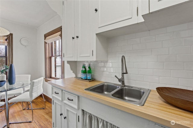 kitchen featuring light wood-type flooring, backsplash, sink, butcher block countertops, and white cabinetry