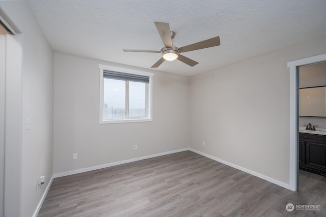 unfurnished room featuring ceiling fan, sink, light hardwood / wood-style floors, and a textured ceiling