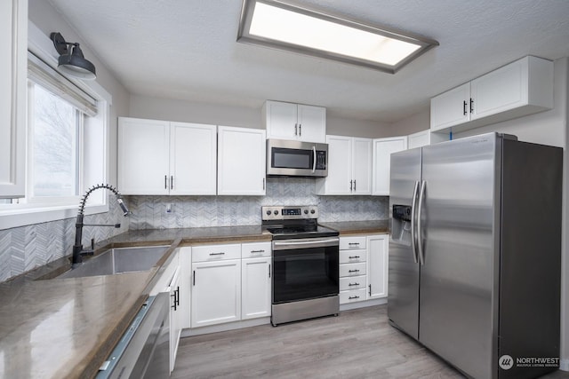 kitchen with white cabinetry, sink, stainless steel appliances, and light hardwood / wood-style floors