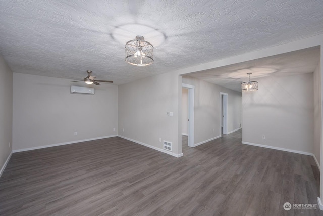 unfurnished room featuring a textured ceiling, ceiling fan with notable chandelier, dark wood-type flooring, and a wall mounted AC