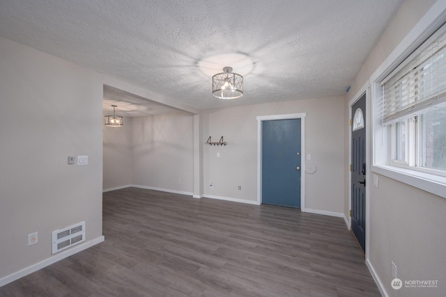 empty room featuring a textured ceiling, dark hardwood / wood-style flooring, and an inviting chandelier