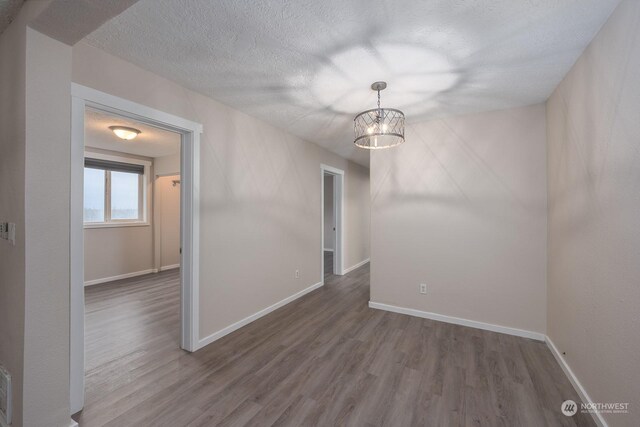 unfurnished room with a notable chandelier, dark hardwood / wood-style floors, and a textured ceiling