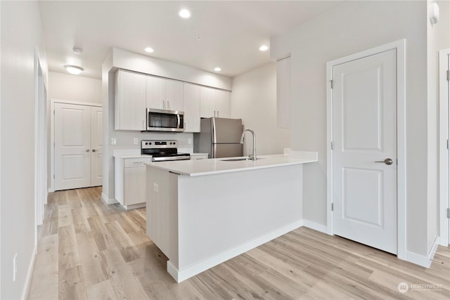 kitchen with kitchen peninsula, appliances with stainless steel finishes, light hardwood / wood-style flooring, and sink