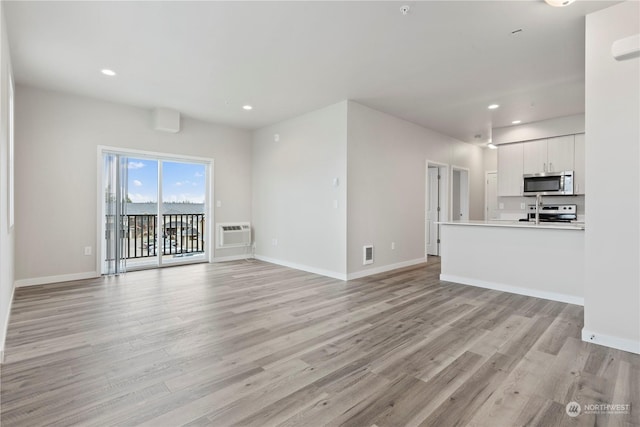 unfurnished living room with a wall mounted air conditioner and light wood-type flooring