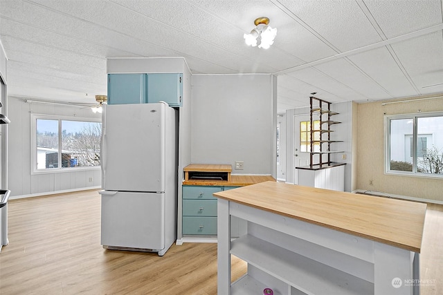 kitchen featuring wooden walls, white fridge, ceiling fan, and light hardwood / wood-style floors