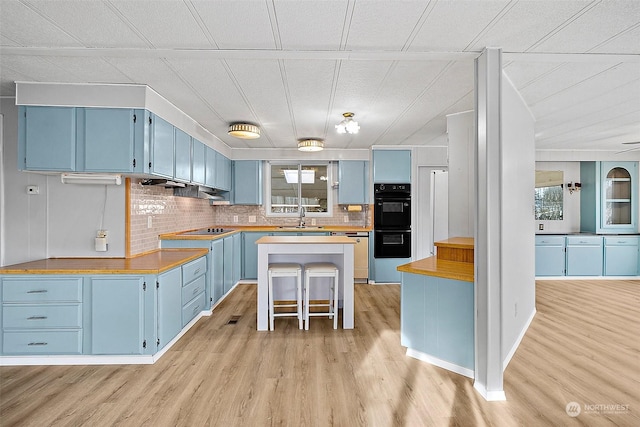 kitchen with a kitchen breakfast bar, light wood-type flooring, sink, blue cabinetry, and a center island