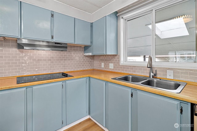 kitchen with blue cabinetry, sink, light hardwood / wood-style floors, black electric cooktop, and decorative backsplash