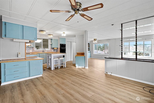 kitchen featuring black oven, light hardwood / wood-style floors, wooden counters, and blue cabinets