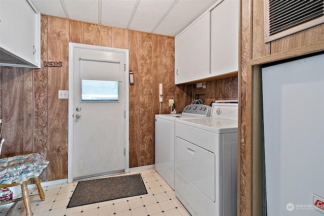 laundry area with cabinets, wooden walls, and washing machine and clothes dryer