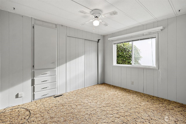 unfurnished bedroom with carpet flooring, ceiling fan, wooden walls, and a textured ceiling