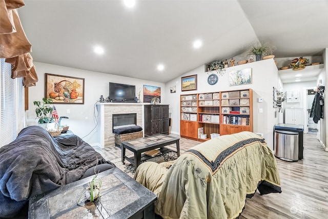 living room featuring a stone fireplace, lofted ceiling, and light hardwood / wood-style flooring