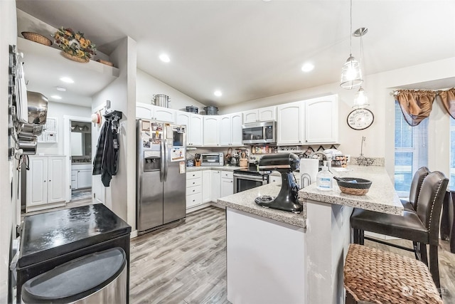 kitchen featuring appliances with stainless steel finishes, pendant lighting, white cabinetry, a kitchen bar, and kitchen peninsula