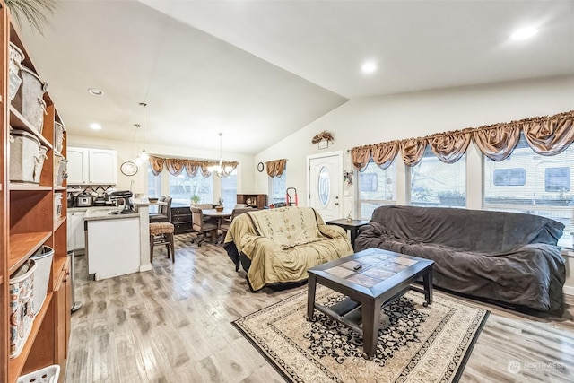 living room with an inviting chandelier, vaulted ceiling, and light hardwood / wood-style flooring