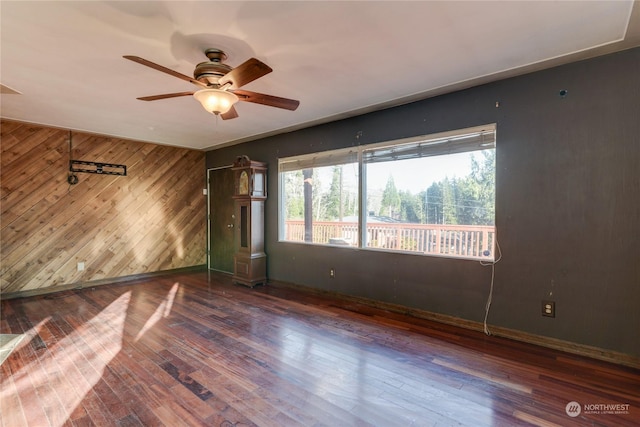 spare room featuring ceiling fan, dark hardwood / wood-style flooring, and wood walls