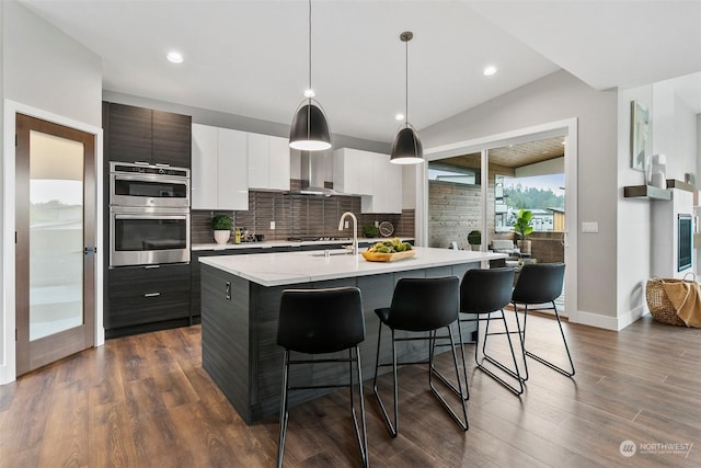 kitchen featuring white cabinets, dark hardwood / wood-style flooring, lofted ceiling, and an island with sink