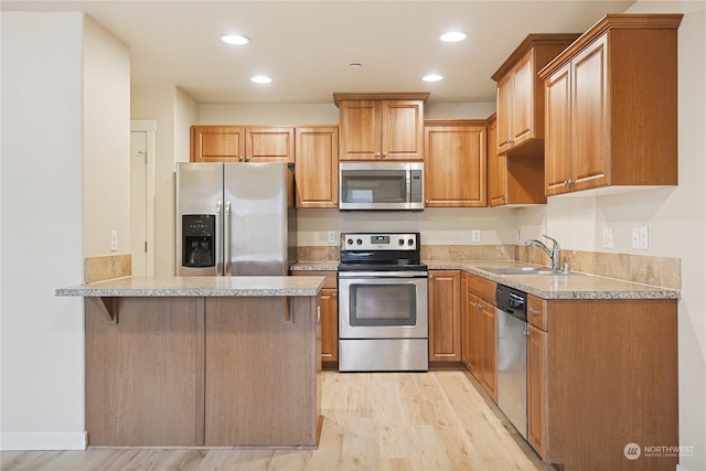 kitchen with a breakfast bar, sink, light hardwood / wood-style flooring, kitchen peninsula, and stainless steel appliances