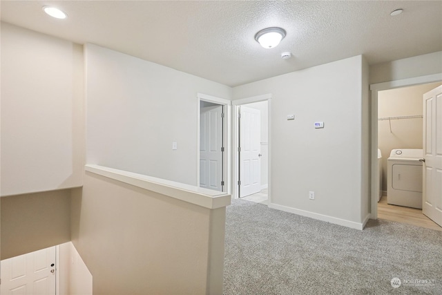 hallway with light carpet, washer / dryer, and a textured ceiling