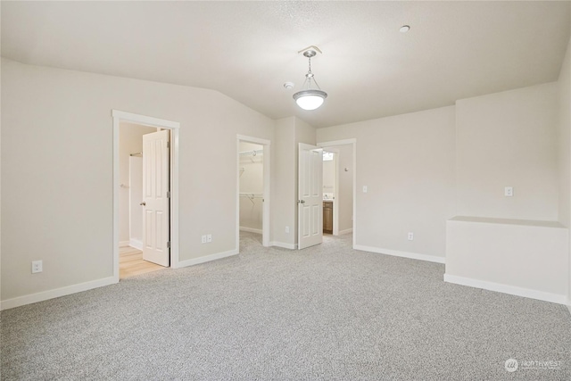 unfurnished bedroom with light carpet, ensuite bath, vaulted ceiling, a spacious closet, and a closet