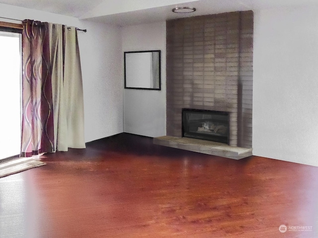 unfurnished living room featuring wood-type flooring and a brick fireplace