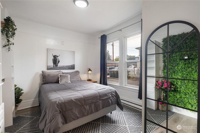 bedroom featuring multiple windows, wood-type flooring, and a baseboard radiator