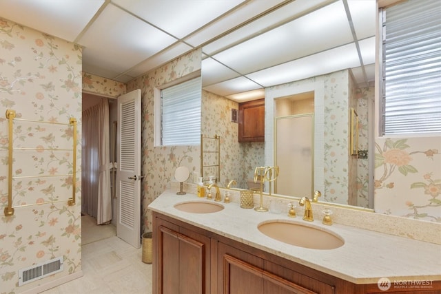 full bath with a sink, visible vents, double vanity, and wallpapered walls