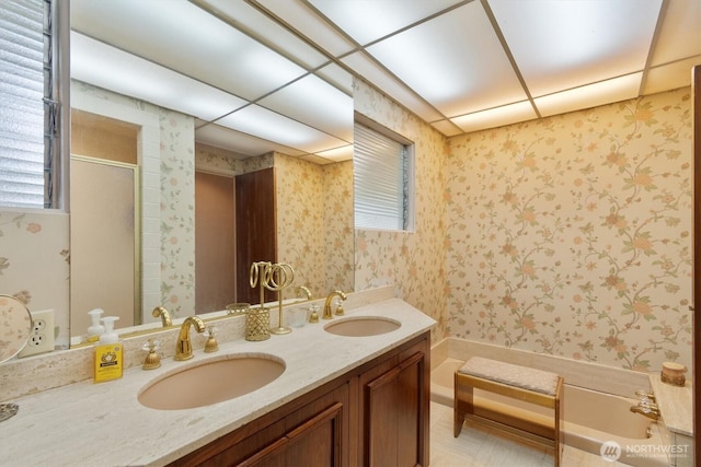 bathroom featuring double vanity, a washtub, wallpapered walls, and a sink