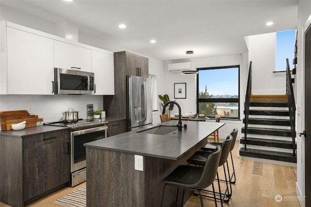 kitchen with dark brown cabinetry, stainless steel appliances, sink, white cabinets, and an island with sink