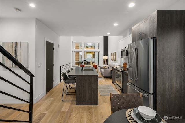 kitchen featuring dark brown cabinetry, a kitchen breakfast bar, light hardwood / wood-style floors, a kitchen island, and appliances with stainless steel finishes