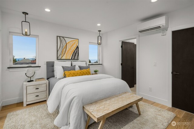 bedroom with a wall unit AC, multiple windows, and light wood-type flooring