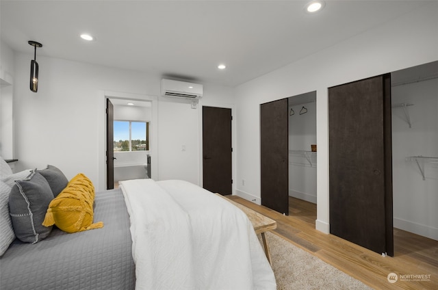 bedroom with connected bathroom, a wall mounted AC, and light wood-type flooring