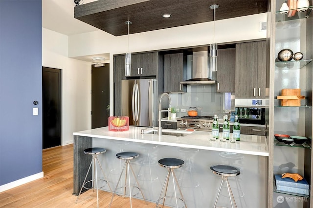 kitchen featuring a kitchen breakfast bar, light hardwood / wood-style floors, stainless steel fridge, dark brown cabinetry, and wall chimney range hood