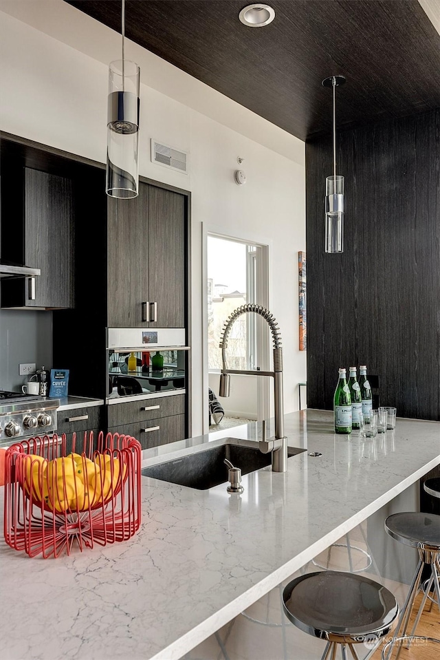 kitchen featuring pendant lighting, stainless steel gas stovetop, a kitchen bar, light stone counters, and sink