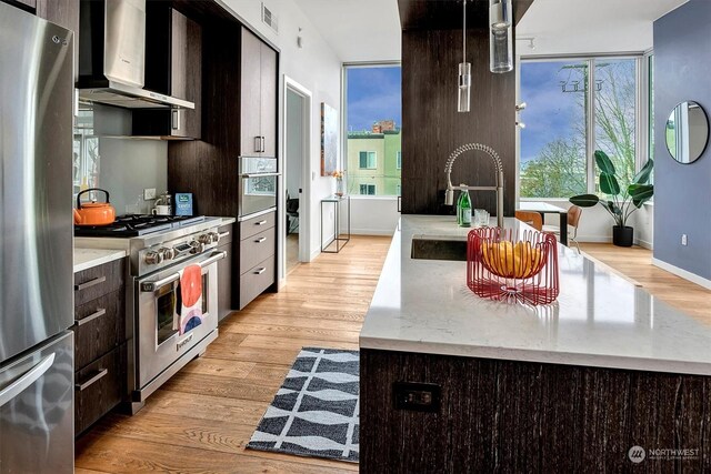 kitchen with stainless steel appliances, sink, a center island, wall chimney exhaust hood, and dark brown cabinets