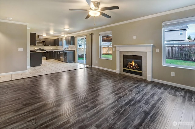 unfurnished living room featuring ceiling fan, light wood-type flooring, ornamental molding, and a tiled fireplace